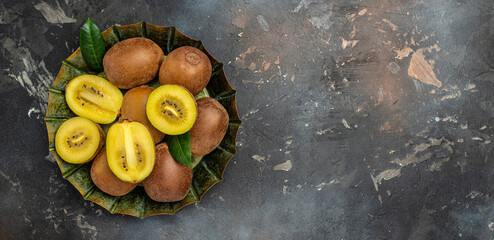 fresh golden kiwi on plate on a dark background, Long banner format. top view
