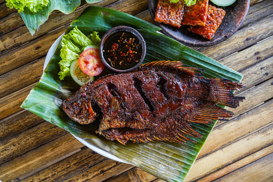 Grilled gurami or grilled gurame with red barbecue sauce, vegetables and chili sauce served on banana leaves,