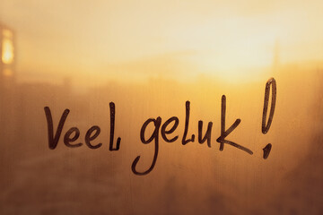 Fototapeta premium Lettering Netherlandish language text Veel geluk is Good luck in english message written finger on foggy glass wet sunset window
