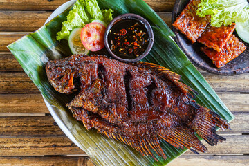 Grilled gurami or grilled gurame with red barbecue sauce, vegetables and chili sauce served on banana leaves,