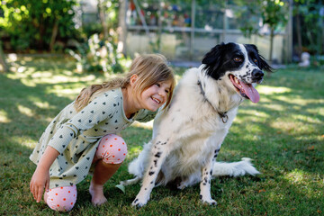 Cute little preschool girl playing with family dog in garden. Happy smiling child having fun with dog, hugging and playing. Friendship and love between animal and kids