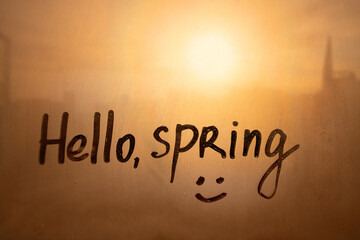 Handwritten text Hello spring and smile on wet orange window