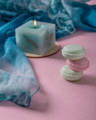 Three crookedly stacked macarons, a lit candle and a scarf, all characterized by delicate pastel...