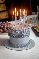 Beautiful silver cake with cream and a 6 burning candles is on the table, a childrens birthday, vertical photo, selective focus.