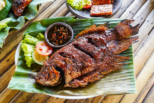Grilled gurami or grilled gurame with red barbecue sauce, vegetables and chili sauce served on banana leaves,