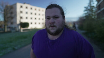 Tracking shot of a fat young man runner outside in street. Overweight person running outdoors. Losing weight concept