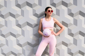 A girl in a pink tracksuit stands with a training ball near the wall © Aleksandr