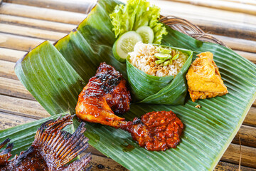 Grilled chicken with red barbecue sauce, vegetables and chili sauce served on banana leaves