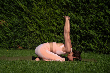 A girl is engaged in yoga on the street, in a pink tracksuit does various exercises and yoga poses