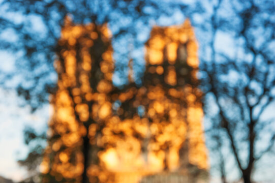 Fine Art photography. Parisi. Blurry photo of Notre Dame cathedral in Paris at sunset. View through tree branches. Bokeh.