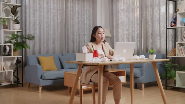 Sick Asian Businesswoman Holding A Thermometer To The Video Call With Doctor On A Laptop While Working At Home
