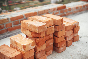 Stack of red bricks on concrete foundation, process of house building. Concrete foundation with...