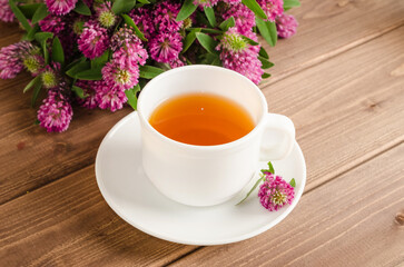 Healthy herbal tea with clover in a white cup on a brown wooden background with a bouquet of clover