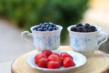 Blueberries, blackberries and strawberries in the vintage porcelain set. Healthy snack served in a garden. Selective focus.