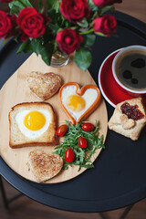 Breakfast on Valentine's Day. Heart shaped scrambled eggs, sausages, toast and cookies and hot coffee or tea, bouquet of red roses 