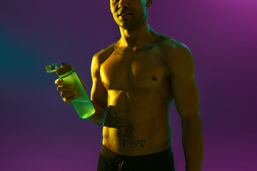 Close up of sporty man with muscled naked torso holding bottle with water on studio background
