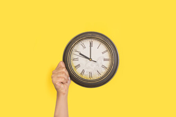 Mano de mujer sosteniendo un reloj sobre un fondo amarillo liso y aislado. Vista de frente y de cerca. Copy space