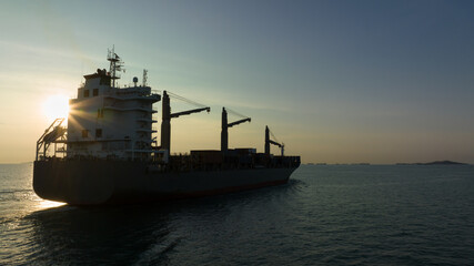 Fototapeta premium corgo ship container in silhouette and over the sunlight at evening in open sea. aerial view