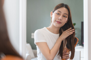 Happy asian woman brushing hair by wooden comb in the morning.