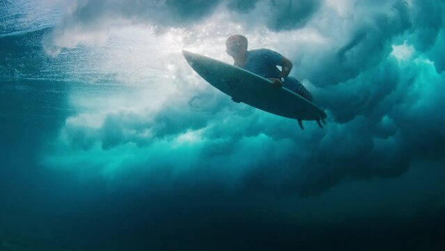Surfer underwater. Man dives under the wave with surfboard to pass the wave. Underwater view of the surfer duck diving under the wave