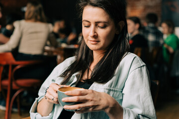 Close-up of a beautiful brunette woman drinking coffee in a coffee shop.
