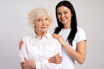 Happy brunette woman hugging with her lovely senior mother isolated on white wall background. Family relationships concept