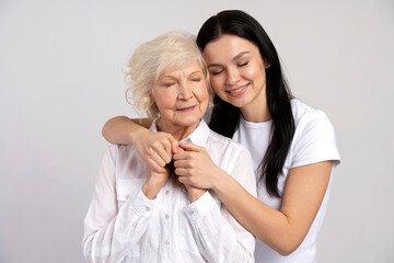Happy brunette woman hugging with her lovely senior mother isolated on white wall background. Family relationships concept
