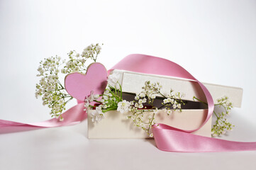 Gift box with a pink painted heart shape, a ribbon and white gypsophila flowers as romantic greeting card for holidays, light background, copy space, selected focus, narrow depth of field