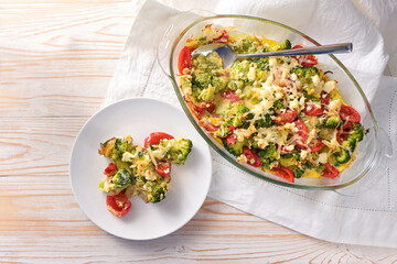 Casserole from vegetables with broccoli, tomatoes, onions, feta and cheese, healthy low carb meal on a light wooden table, copy space, high angle view from above