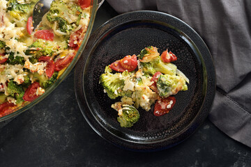 Vegetable dish from baked broccoli, tomatoes, onions, feta and cheese served on a dark plate, copy space, high angle view from above, selected focus