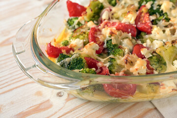Part of a vegetable casserole dish baked with broccoli, tomatoes, onions, feta and cheese, hot and fresh from the oven on a light wooden table, copy space, selected focus