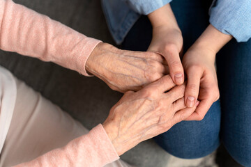 Top view of the mature female aged wrinkled skin and hands of her care giver. Senior woman in elderly care facility gets help from hospital personnel nurse. Grand mother everyday life concept