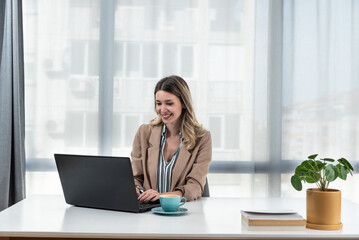 Young happy satisfied successful businesswoman manager and executive sitting in office casually working on laptop computer enjoying working day self-conscious and grateful for success and hard work