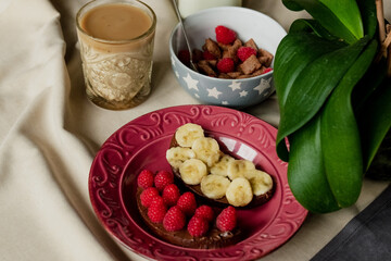 breakfast, cereal with milk, coffee with milk in a faceted glass, beterbrots with chocolate butter, berries and bananas