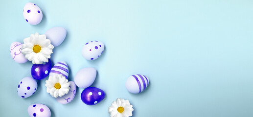 Easter holiday background with colorful easter eggs and white flowers on blue background. Top view from above.