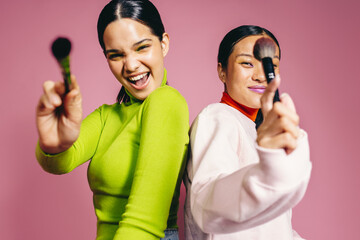 Radiant 20s: Two vibrant young women having fun holding makeup brushes in a studio