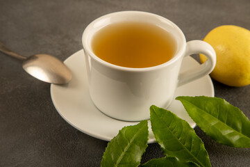 A cup of green tea, tea leaves and lemons, on black background
