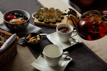 Girl pours black tea into a cup for breakfast