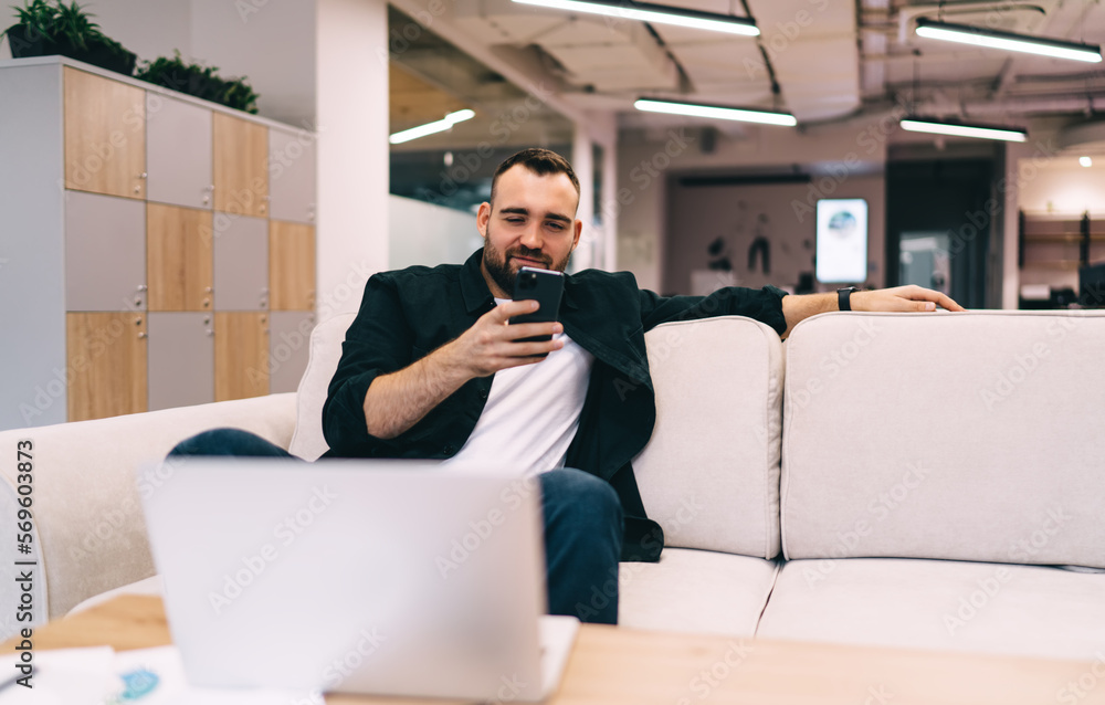 Poster smiling man using smartphone while sitting on sofa in office