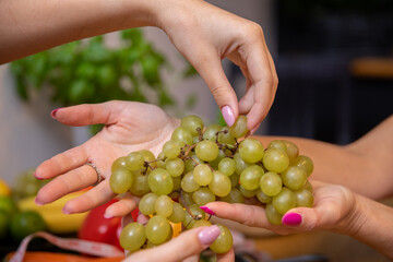 Close-up on the hands of two women handing each other a bunch of grapes - obrazy, fototapety, plakaty