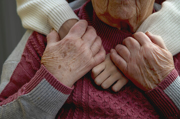 The hands of an old and a young woman embrace each other. Love and care for the older generation,...