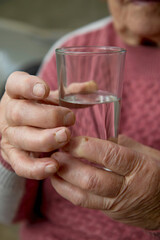 the hands of an elderly woman hold a glass of clean water. The concept of health and proper lifestyle in old and old age