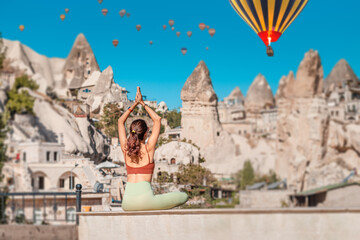 Happy girl does yoga exercises and meditation in Cappadocia, Turkey, with hot air balloons flying in the background