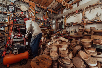 A senior man processing wooden dishes in the workshop in the traditional manual way