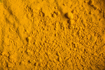 Turmeric powder spread on a flat surface for an uneven landscape with some small stones of that orange spice. Organic texture abstract background.