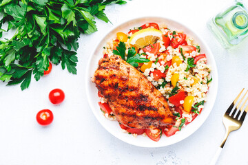 Grilled chicken breast fillet with tabbouleh salad with bulgur, tomato and parsley with lemon dressing, white table background, top view