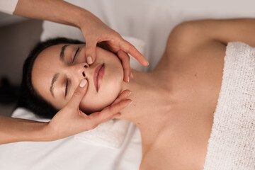 Fototapeta na wymiar Crop masseuse massaging face of client
