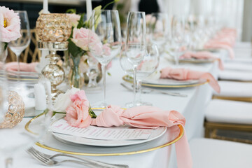 Table service. Close up a plate decorated with pink flowers, a folded napkin and a restaurant menu....