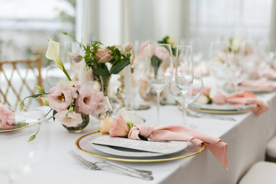 Wedding decorations. Served wedding table with decorative fresh pink flowers and candles. Celebration details. Flower composition roses plates and candles in candlesticks