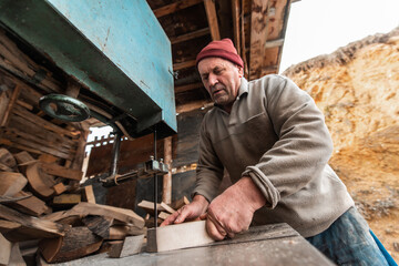 A senior man processing wood on a machine in an outdoor workshop.